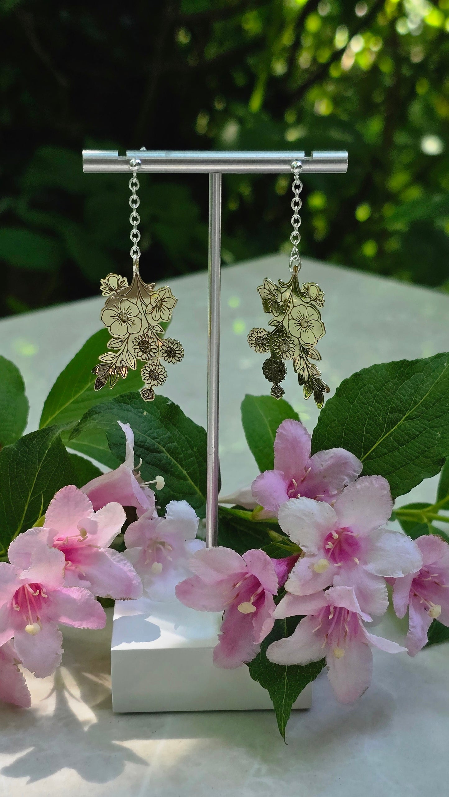 Pair of earrings displayed on a stand with pink flowers and green leaves in the background