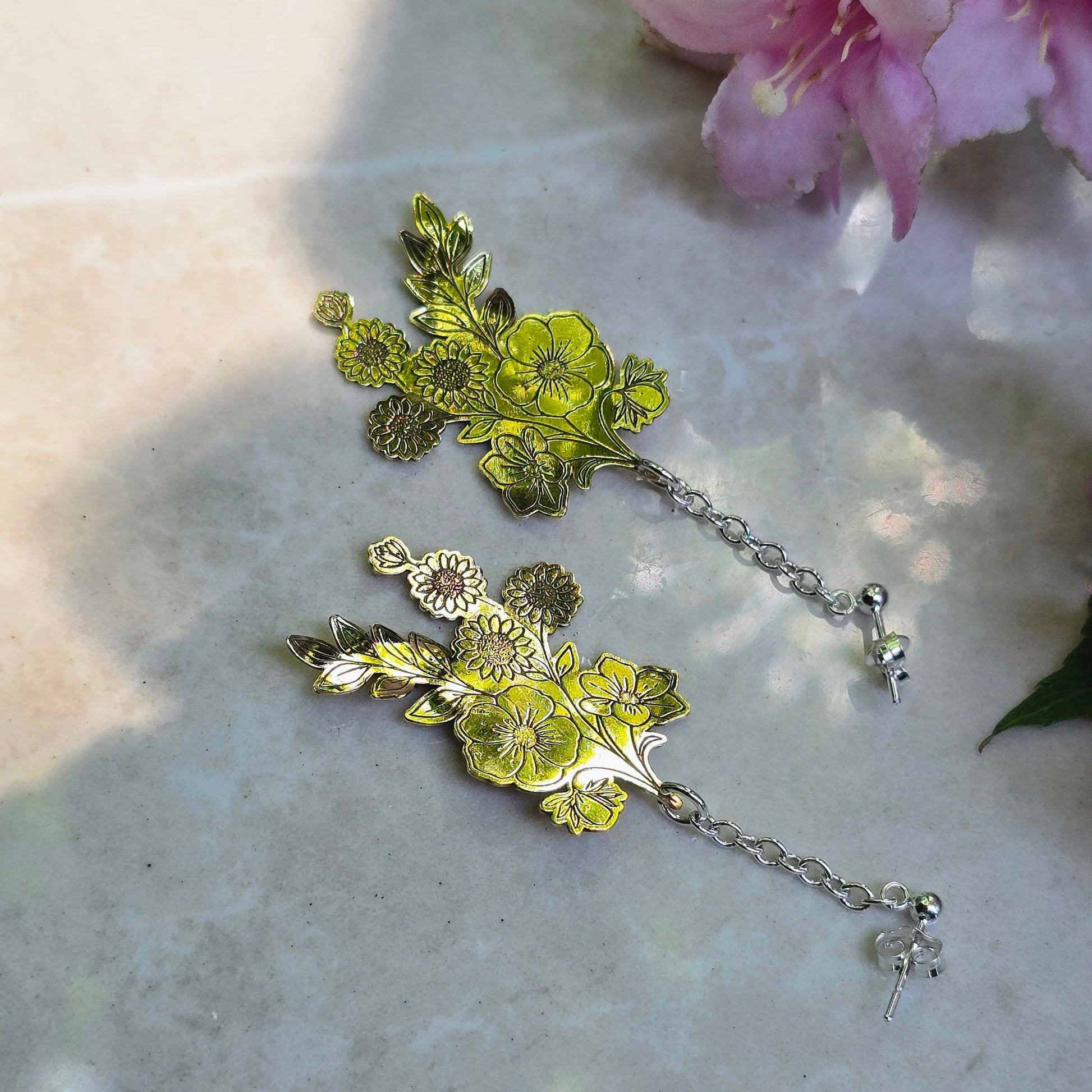 Floral earrings with green and silver details on a light surface with pink flowers.