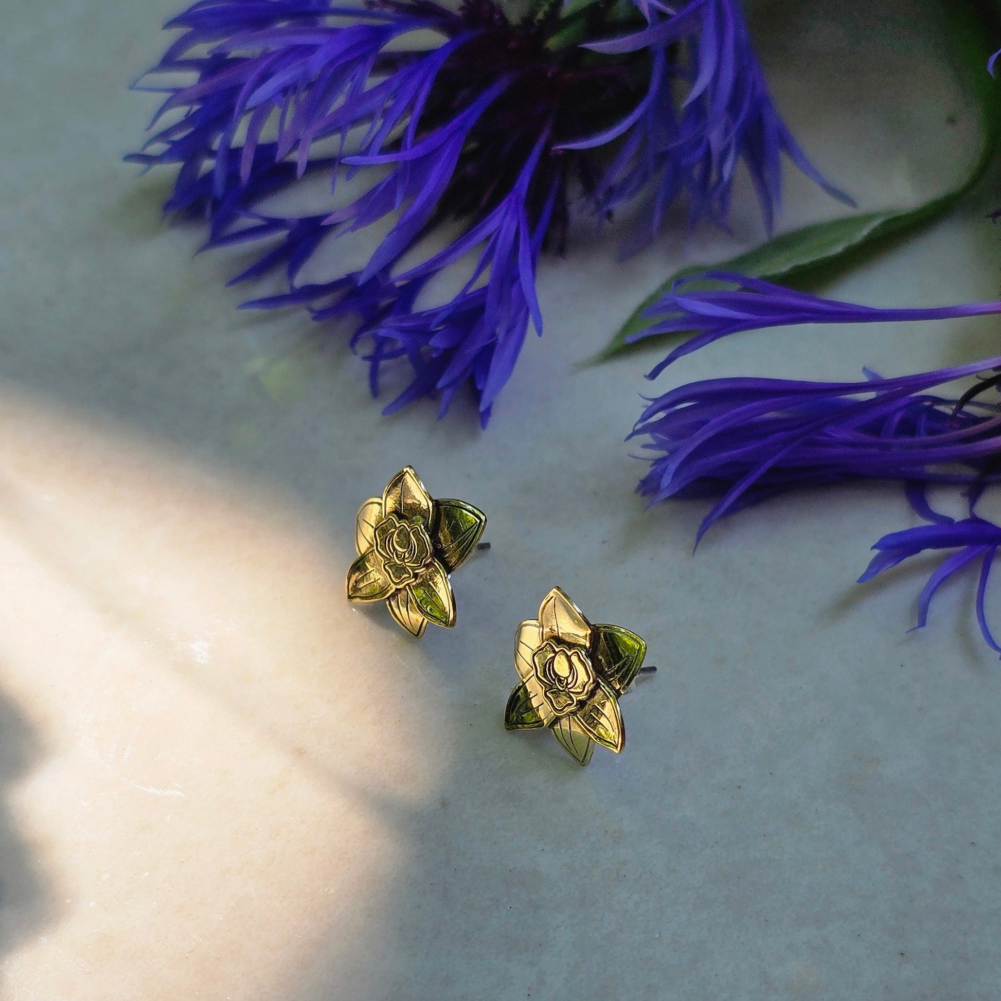 Gold orchid earrings next to blue cornflowers on a textured surface